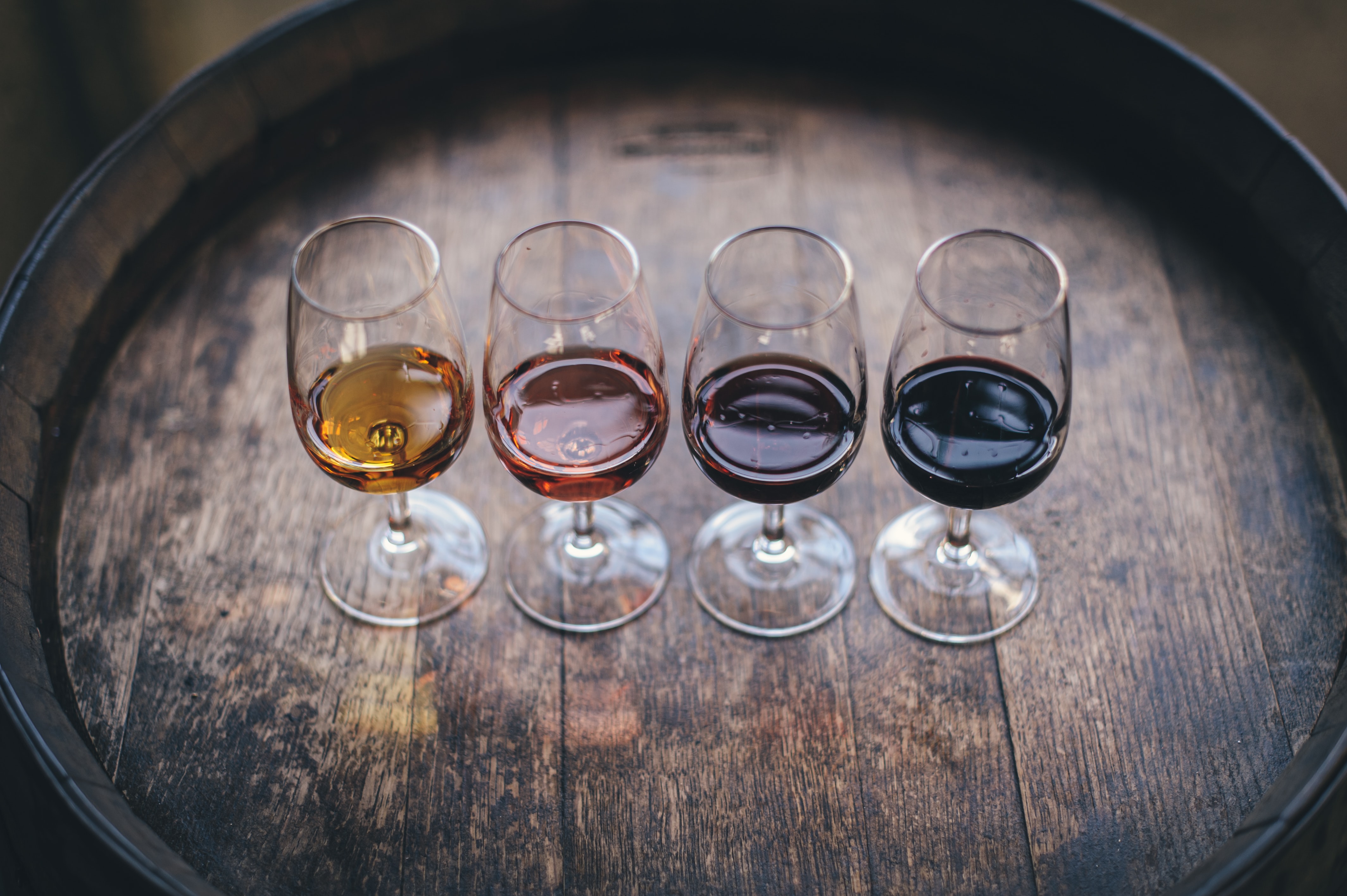 Four wine glasses with wine on top of barrel